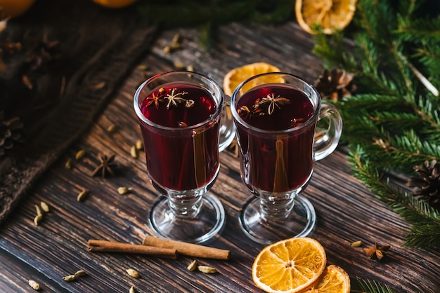 Mulled wine in glass glasses with orange slices, cinnamon sticks and spices with Christmas decor