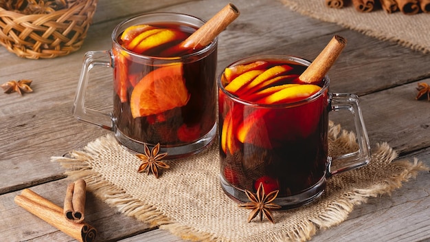 Mulled wine in glass mugs with spices and citrus fruit on an old wooden table