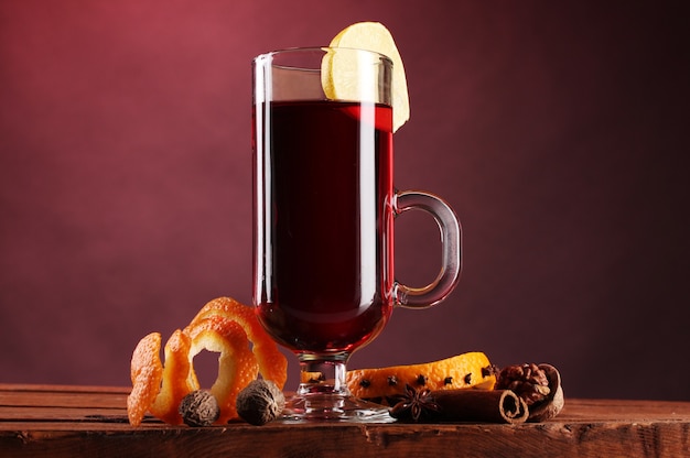 Mulled wine in the glass, spice and lemon on red surface