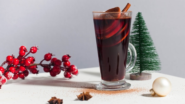 Mulled wine in a glass with a christmas tree a branch with winter red berries photos with hard light...