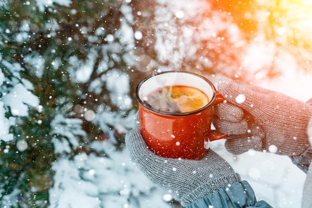숲에서 눈이 내리는 동안 소녀의 손에 든 mulled 와인, 향기로운 겨울 따뜻한 음료...
