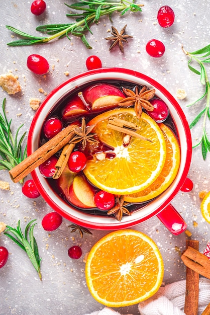 Mulled Wine Hot Drink with Citrus and Spices, Traditional Autumn Winter Warm Alcohol Beverage, in small portioned red stewpan or mug  with Mulled Wine Ingredients - fruit and spices, copy space