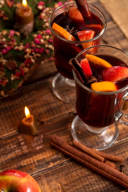 Mulled wine near candle with fruits and spices on wooden table.