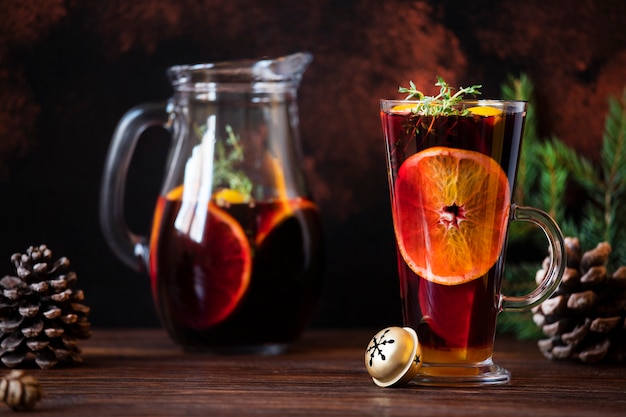 Mulled wine a warm drink made of red wine, citruses and spices on a wooden table with Christmas decorations. Glass and decanter with mulled wine. Dark background. Closeup, colorful, copyspace