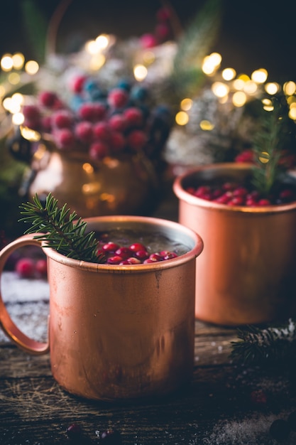 Mulled wine with cranberry in copper mug with christmas decorations on wooden table