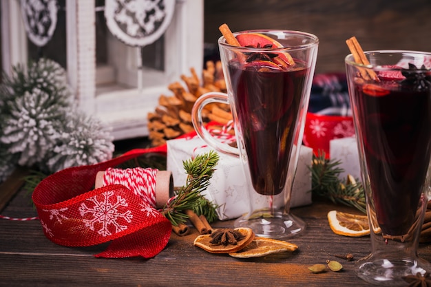 Mulled wine with fruits, cinnamon sticks, anise, decorations and gift boxes on dark wooden  background. Winter warming drink with recipe ingredients. 