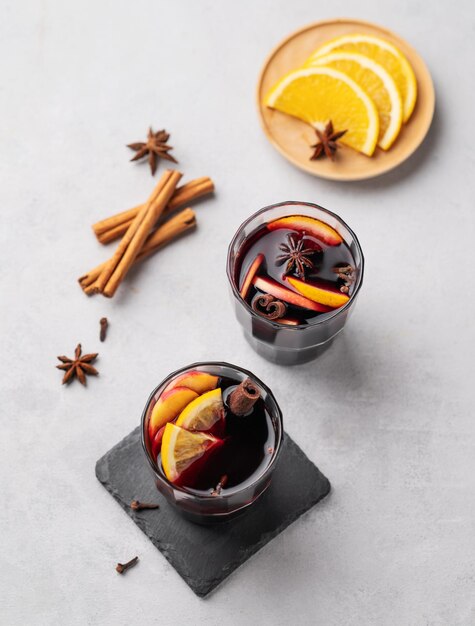 Mulled wine with orange apple and cinnamon in glasses on a light background The concept of a traditional winter hot drink with spices and fruits