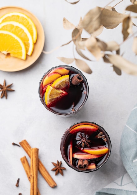 Mulled wine with orange apple and cinnamon in glasses on a light background The concept of a traditional winter hot drink with spices and fruits