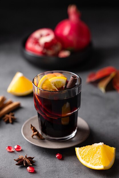 Mulled wine with orange apple pomegranate and cinnamon in glass on a dark background