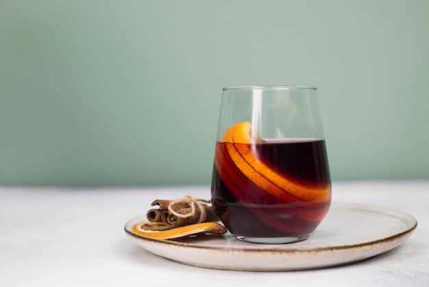 Mulled wine with orange in a glass on a plate on grey and green background