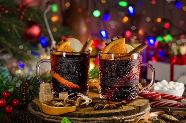 Mulled wine with orange slice, cinnamon stick and spices on the background of festive garland lights. Dark style