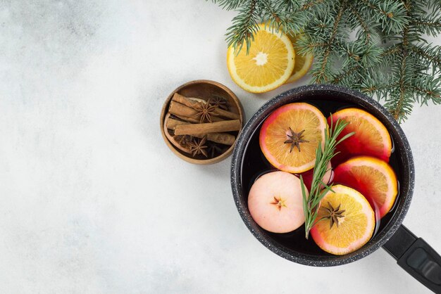 Mulled wine with pieces of orange and apples in a black ladle on a grey background