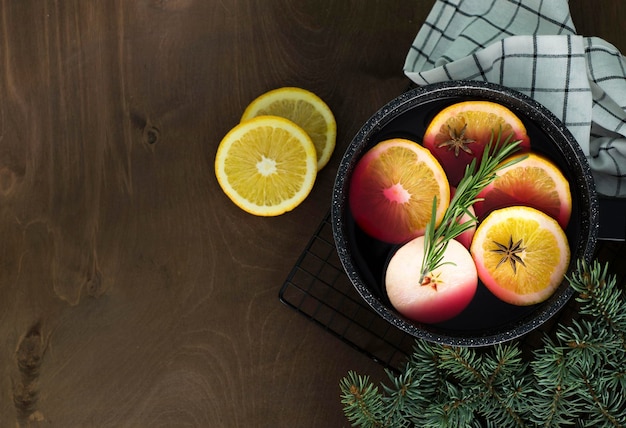 Mulled wine with pieces of orange and apples in a black ladle on a wooden background