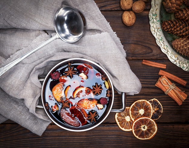 Mulled wine with spices and pieces of fruit in a round aluminum pan