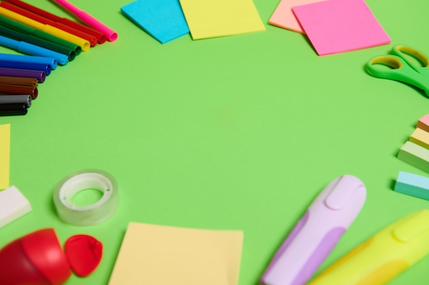 Multi colored assortment of stationery office supplies and school accessories arranged in a circle on light green background, copy space