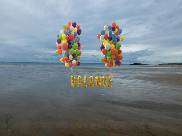 Multi colored balloons on beach against sky