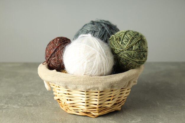 Multi colored balls of yarn in a wicker basket on a light gray background.