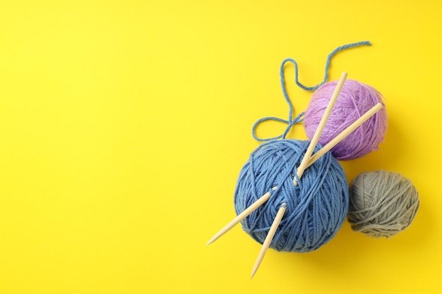 Multi-colored balls of yarn with knitting needles on yellow background.