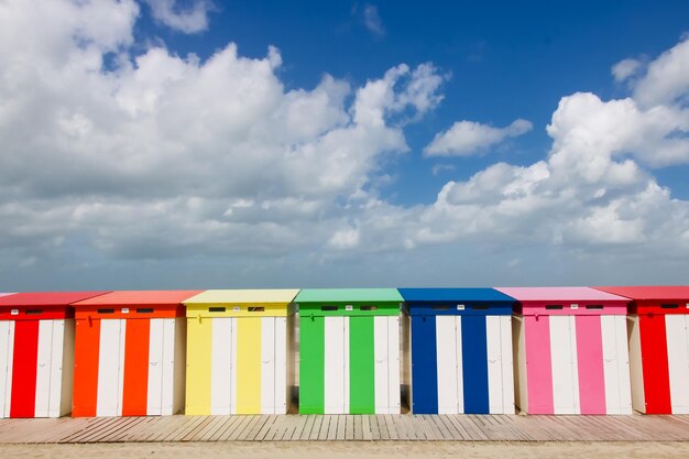 Multi colored beach huts against cloudy sky