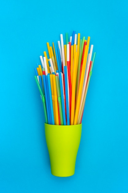 Multi-colored cocktail tubes in a green cup on a blue background