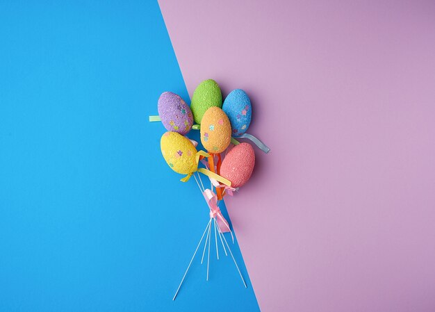 Multi-colored decorative Easter eggs on sticks on a blue lilac surface