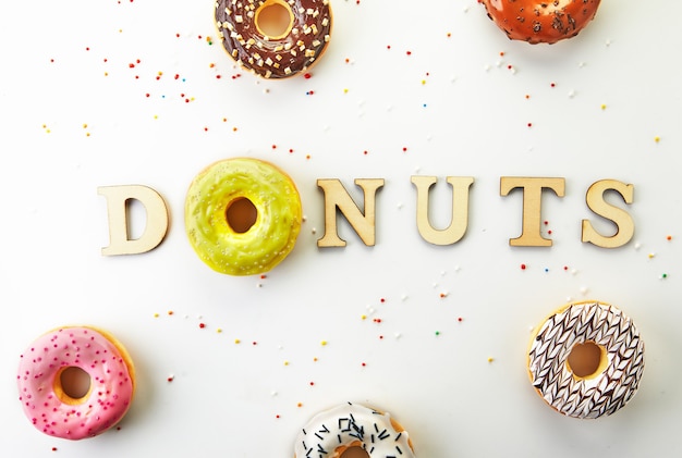 Multi Colored donuts with icing, sprinkles and the inscription donuts on white background. Flat lay