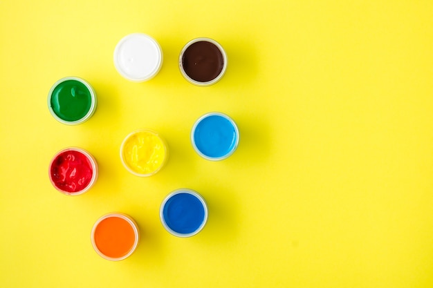 Multi-colored gouache in open jars on a yellow