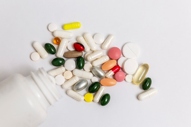 Multi-colored pills spilled out of a white bottle onto a table. Medicine. Close-up. Space for text.