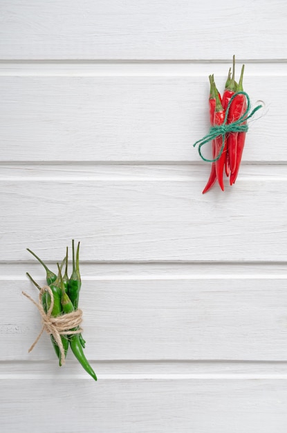 Multi-colored red and green hot chilli peppers tied with a scourge on a white wooden background or table with place for text.