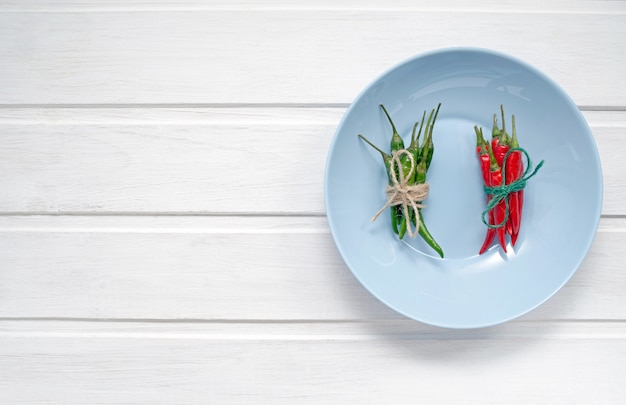 Multi-colored red and green hot chilli peppers tied with a scourge on a white wooden background or table with place for text.