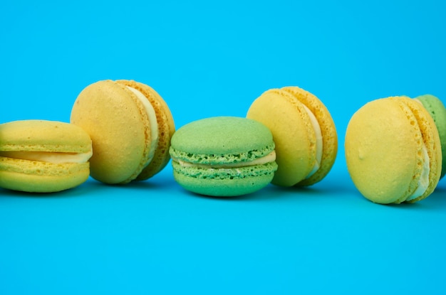 Multi-colored round baked macarons cakes on a light blue background, dessert stands in a row