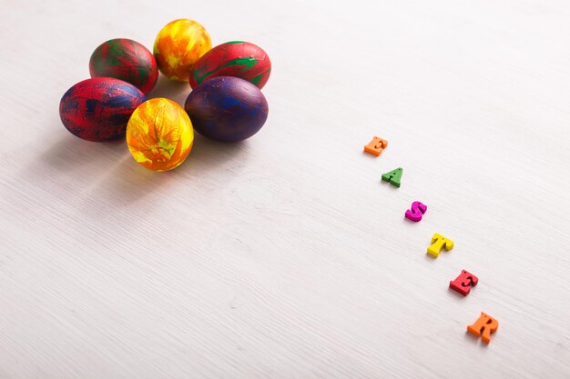 Multi-colored wooden letters making up the words happy easter and decorative colourful eggs on a white background with copy space.