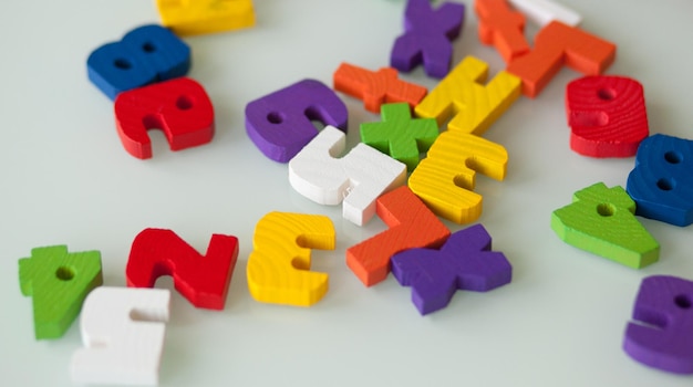 Multi-colored wooden letters and numbers randomly scattered on a white table