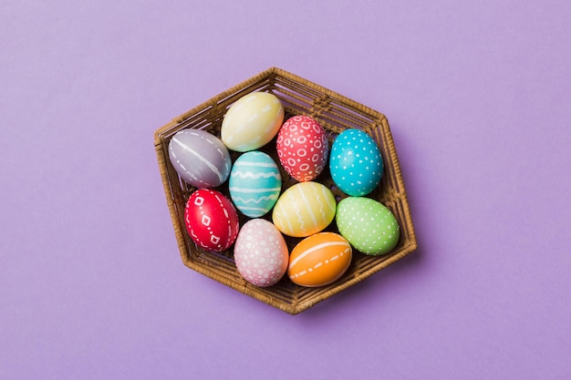 Multi colors easter eggs in the woven basket on colored background pastel color easter eggs holiday concept with copy space