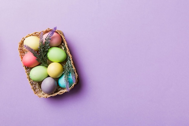 Multi colors easter eggs in the woven basket on colored background pastel color easter eggs holiday concept with copy space