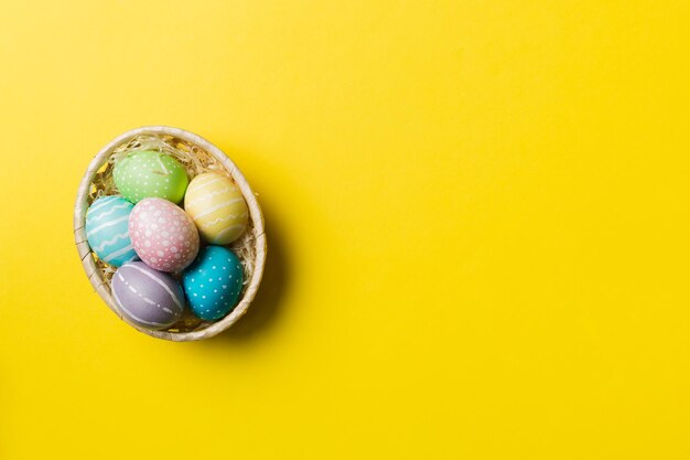 Multi colors Easter eggs in the woven basket on colored background Pastel color Easter eggs holiday concept with copy space