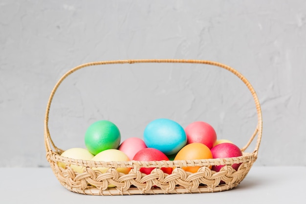 Multi colors Easter eggs in the woven basket on colored background Pastel color Easter eggs holiday concept with copy space