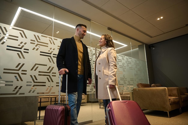 Multi ethnic beautiful couple in love, business partners on\
business trip, standing at the exit of vip meeting room in the\
airport departure terminal, waiting for flight. newlyweds on their\
honeymoon