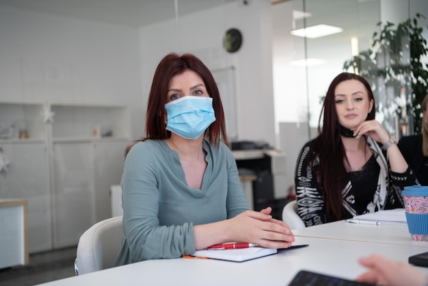 코로나바이러스 발병 시 보호용 의료 마스크를 쓰고 밝은 현대 사무실에서 일하는 다민족 기업인 팀