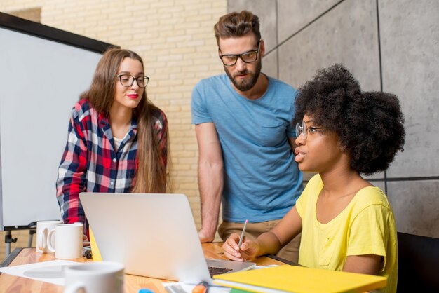 Multi ethnic coworkers dressed casually in colorful clothes talking together sitting with laptop indoors