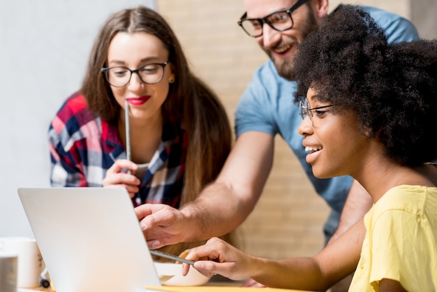 Multi ethnic coworkers dressed casually in colorful clothes working during the meeting at the office with laptop and documents