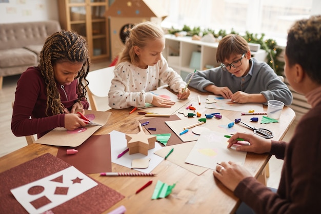 Photo multi-ethnic group of children making handmade christmas cards together while enjoying art and craft class, copy space