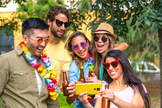 Multi ethnic group of friends partying in the city park taking a selfie smiling looking at the photos on the phone