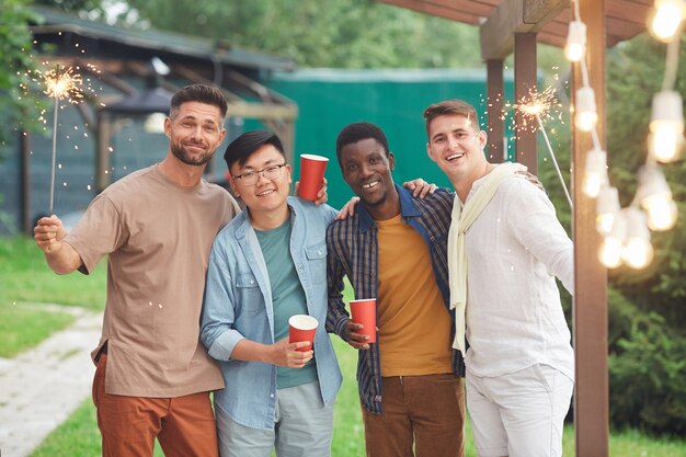 Multi-ethnic group of male friends holding sparklers while enjoying party outdoors