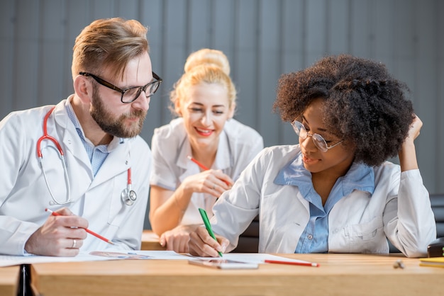 Gruppo multietnico di studenti di medicina in uniforme che discutono seduti insieme nell'aula moderna