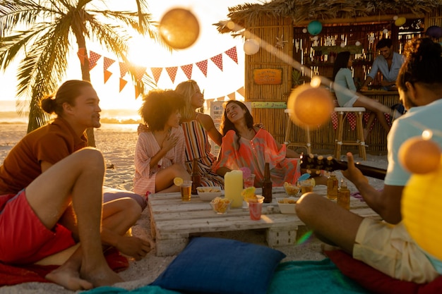 Foto un gruppo multietnico di persone che si divertono in spiaggia con i loro amici durante un tramonto, seduti sulla sabbia, suonando la chitarra e sorridendo