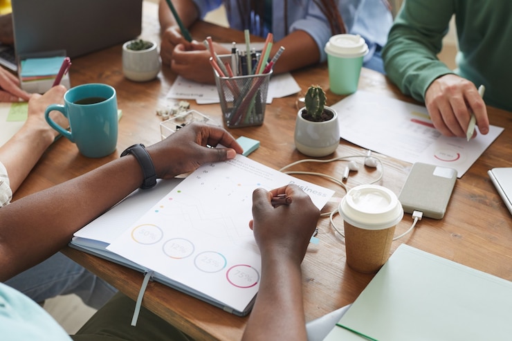 Photo multi-ethnic group of people working together at cluttered table with cups, mugs and stationary items, teamworking or studying concept