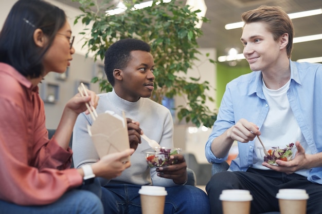 테이크 아웃 음식을 먹고 학교 또는 사무실에서 점심 시간 동안 웃고있는 젊은 사람들의 다민족 그룹