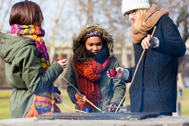 Multi-ethnic group of young people roasting sausages outdoors in a cold day of Autumn