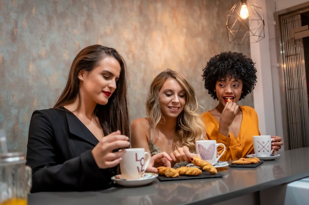 Multi-ethnic lifestyle of three girlfriends having coffee and cookies in a coffee shop